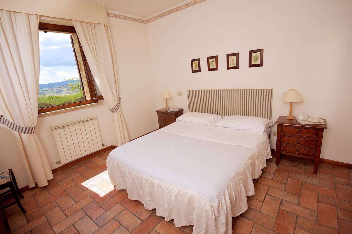 A bedroom with a large bed, two bedside tables, a window with curtains, and a radiator.
