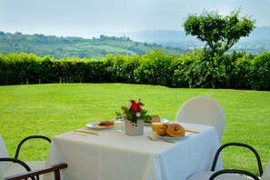 Une table dressée à l’extérieur, avec vue sur des collines ondoyantes et un arbre en arrière-plan.