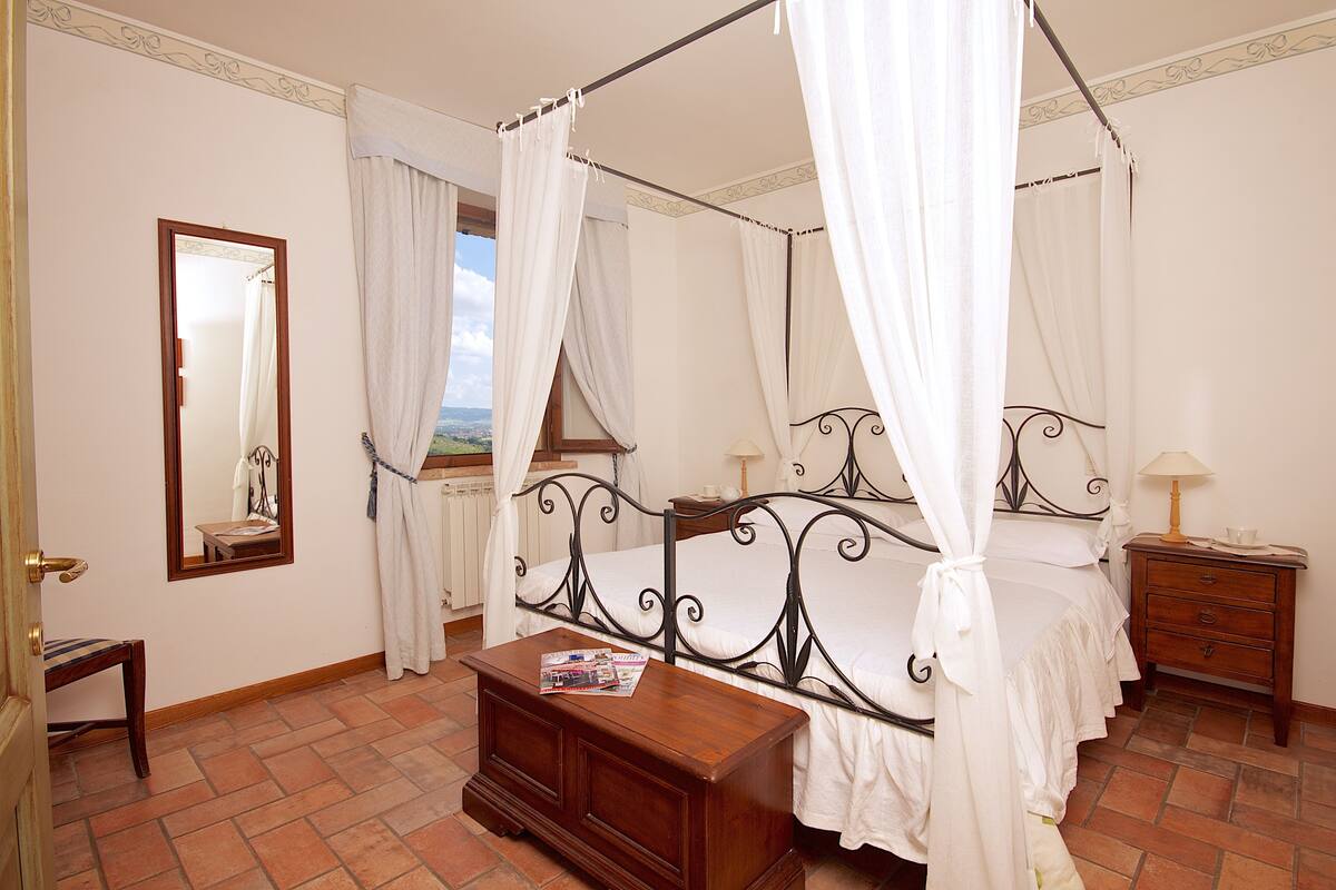 A four-poster canopy bed with a wooden nightstand and a mirror on the wall.