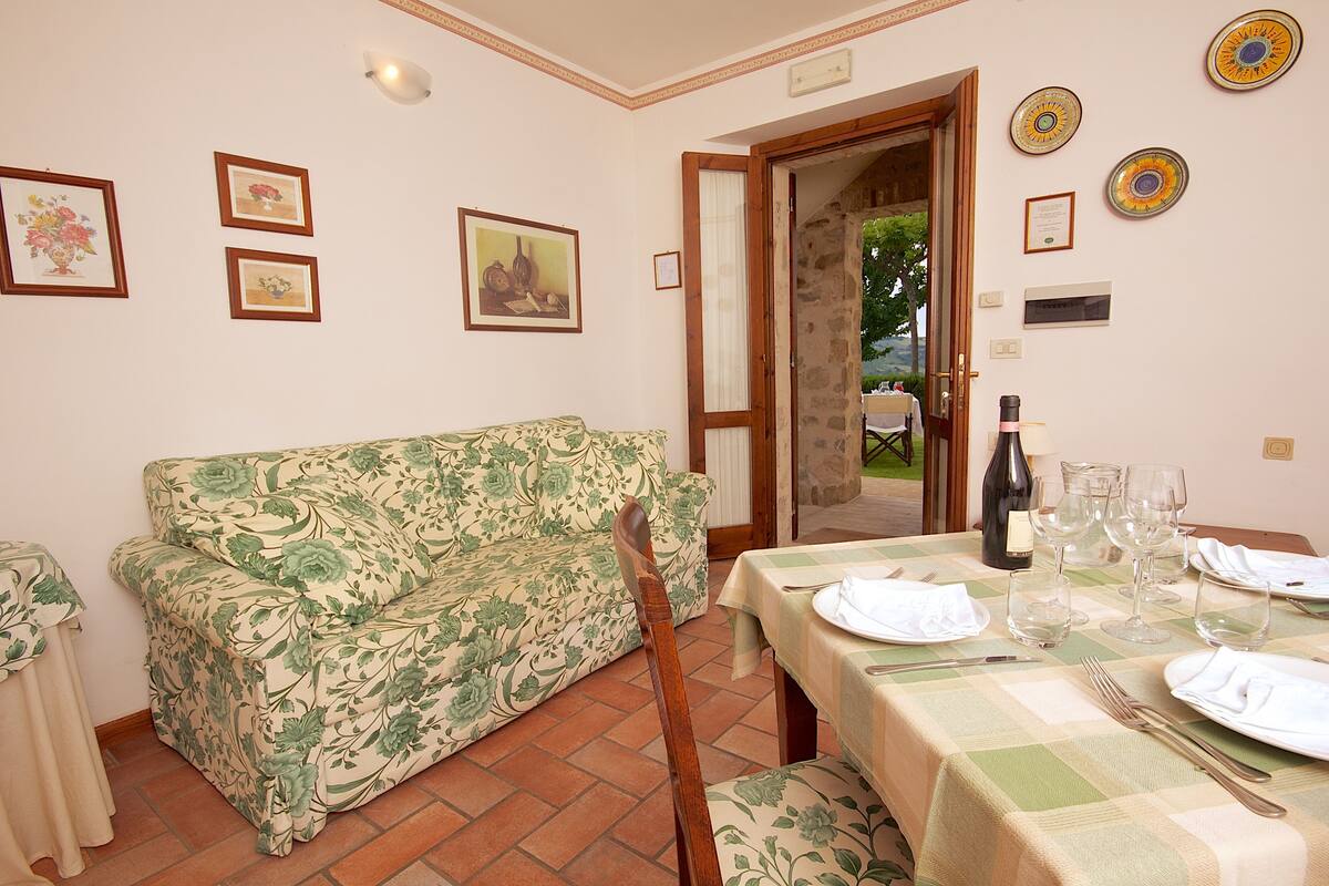 A dining area with a table set for two, a floral sofa, and a wine bottle.