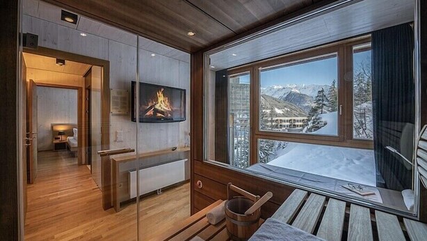Une pièce chaleureuse avec une cheminée, une grande fenêtre donnant sur les montagnes et un banc en bois.