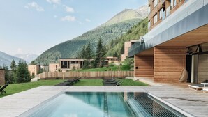 Un espace piscine extérieur moderne, doté d’une terrasse en bois, de chaises longues et offrant une vue sur une chaîne de montagnes.