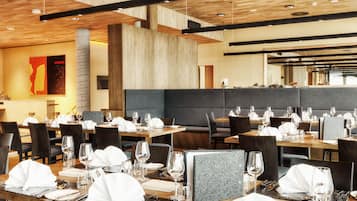A modern restaurant with wooden tables and chairs, a high ceiling with exposed beams, and a large seating area.