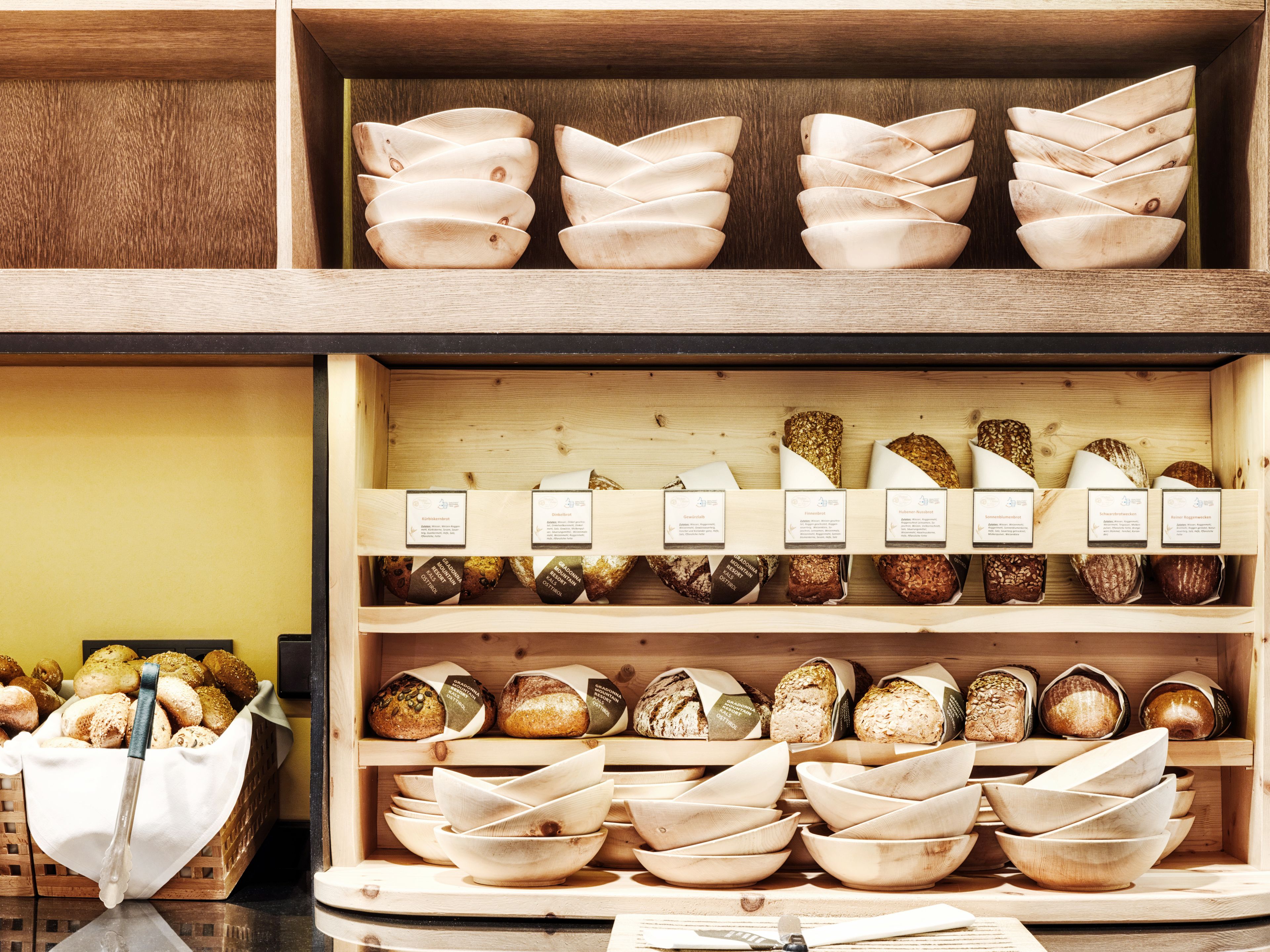 Een bakkerijvitrine met verschillende broden en houten kommen.