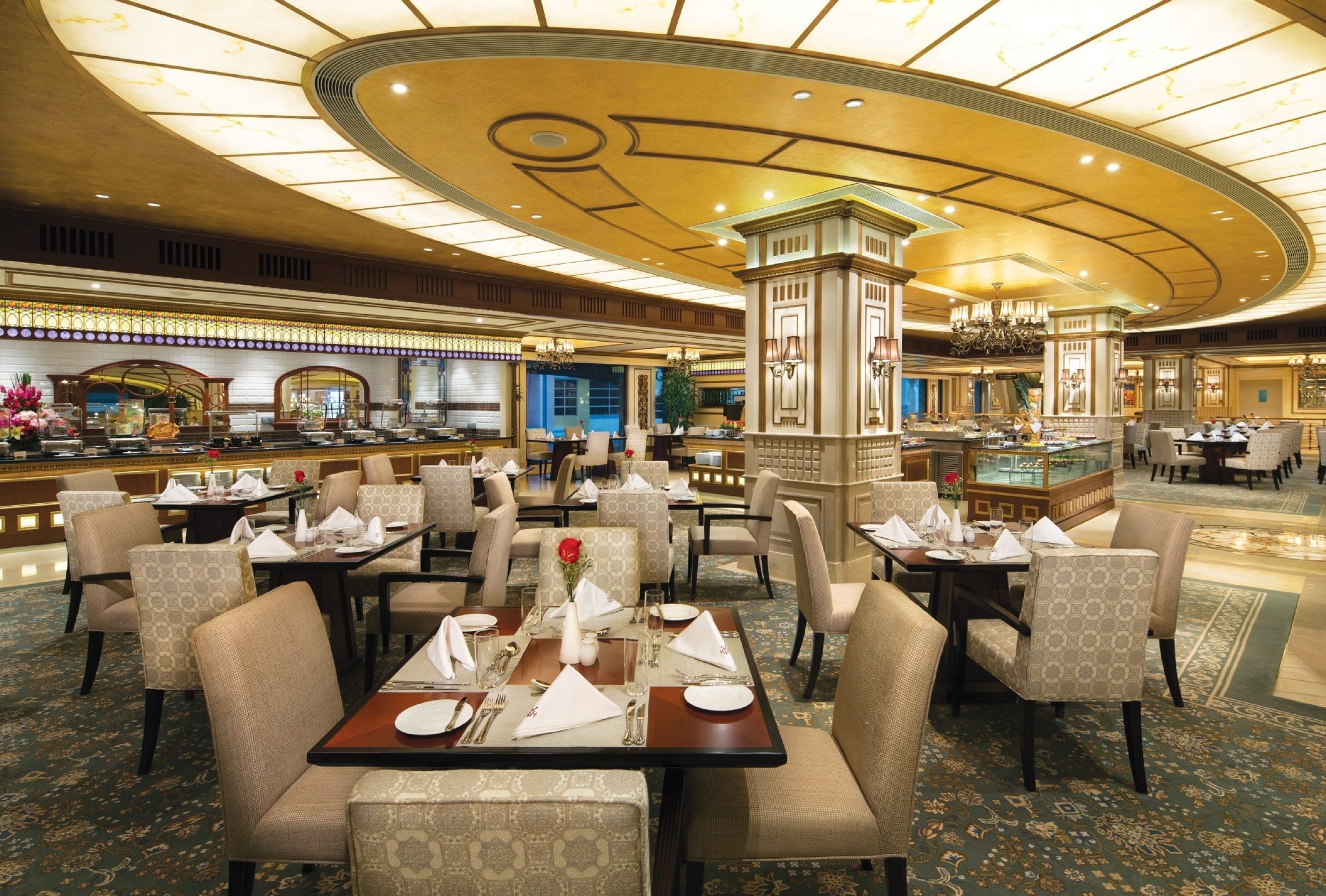 A spacious hotel lobby with multiple dining areas, a central decorative pillar, and a well-lit ceiling.