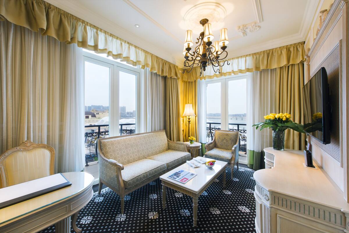 Ein Hotelzimmer mit Sofa, Sesseln, Couchtisch, Fernseher und einem Balkon mit Blick.