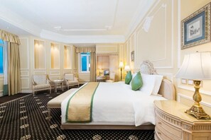 Habitación de hotel con una cama grande, dos sillones, una mesita y una mesita de noche con lámpara.