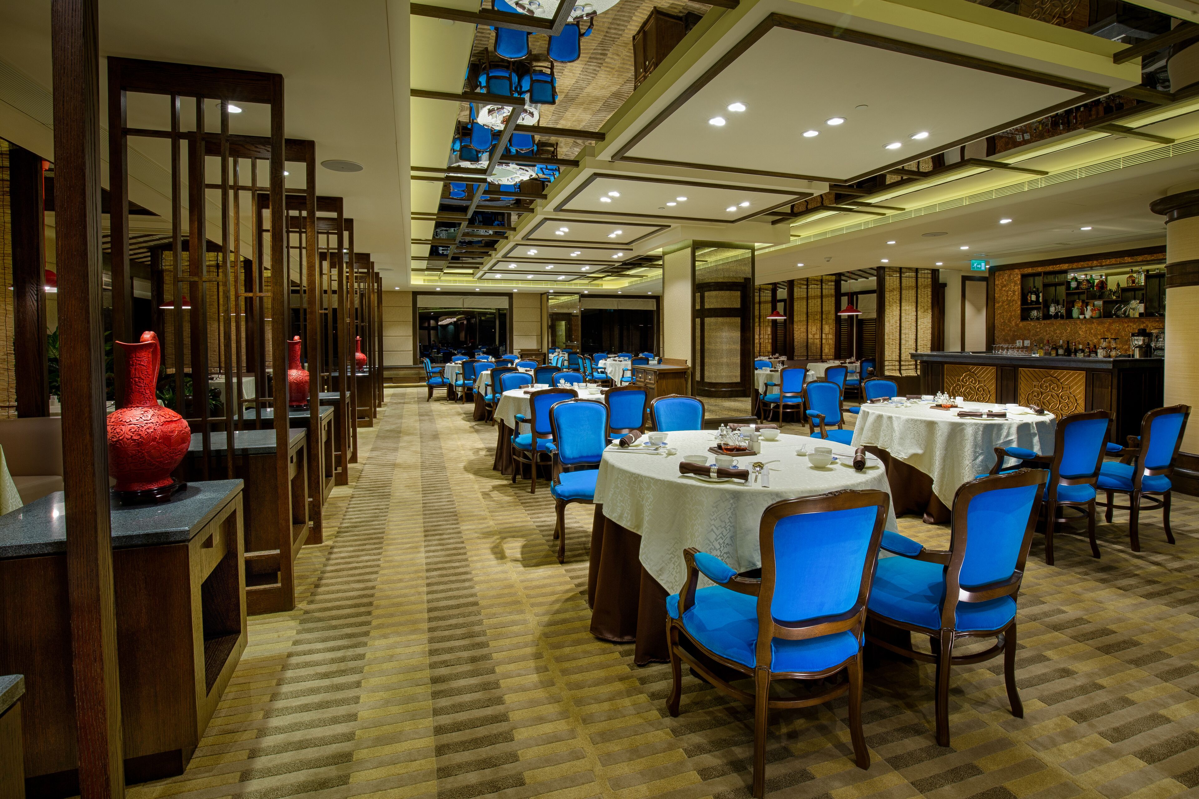 A hotel dining area with multiple round tables, blue chairs, and a bar counter.