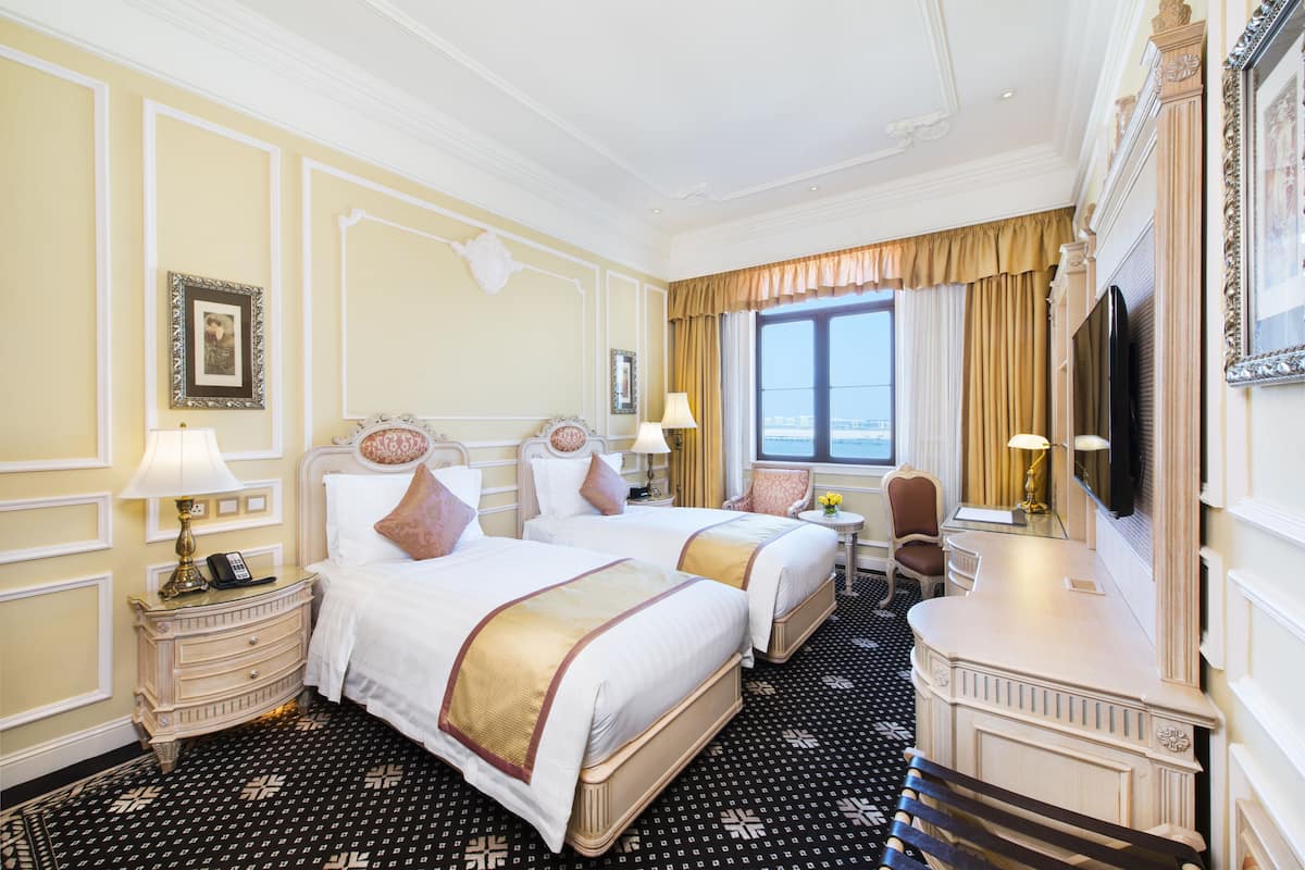 Ein Hotelzimmer mit zwei Betten, einem Schreibtisch, einem Sessel, einem Fernseher und einem Fenster mit Vorhängen.