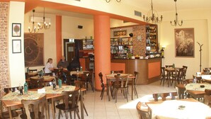 A restaurant with multiple tables and chairs, a bar area with shelves of bottles, and a clock on the wall. - Rezidence Davids (Prague)