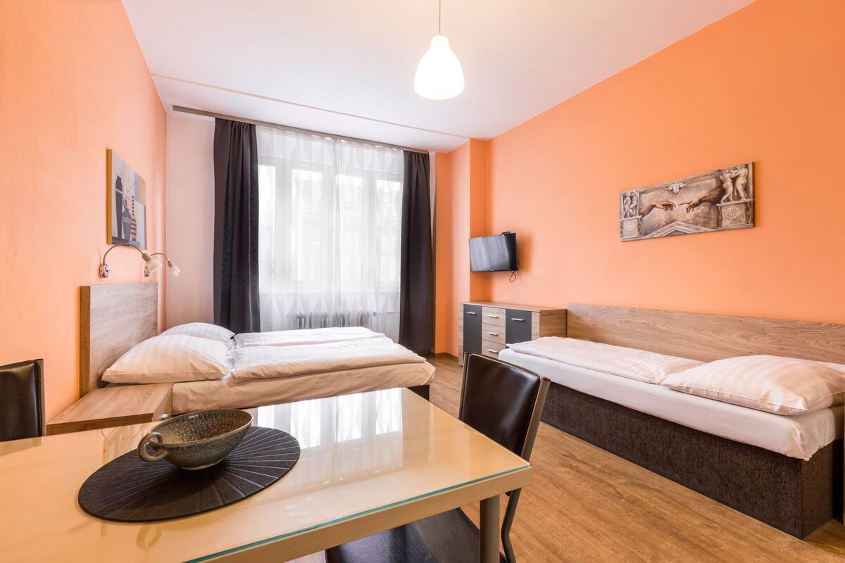 Une chambre d’hôtel avec deux lits, une table à manger, un téléviseur et une fenêtre avec des rideaux.