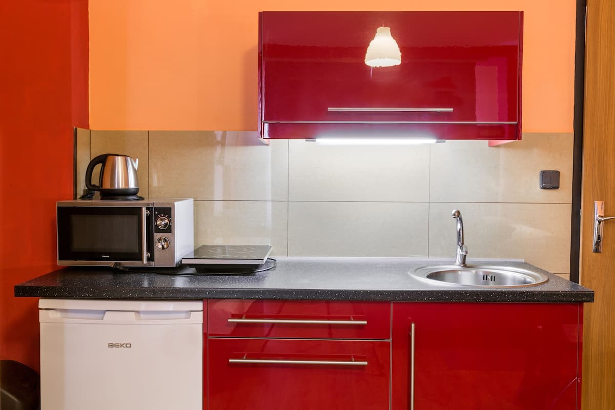 Une cuisine compacte équipée d’un four à micro-ondes, d’une bouilloire et d’un évier, avec des meubles rouges et un plan de travail noir.