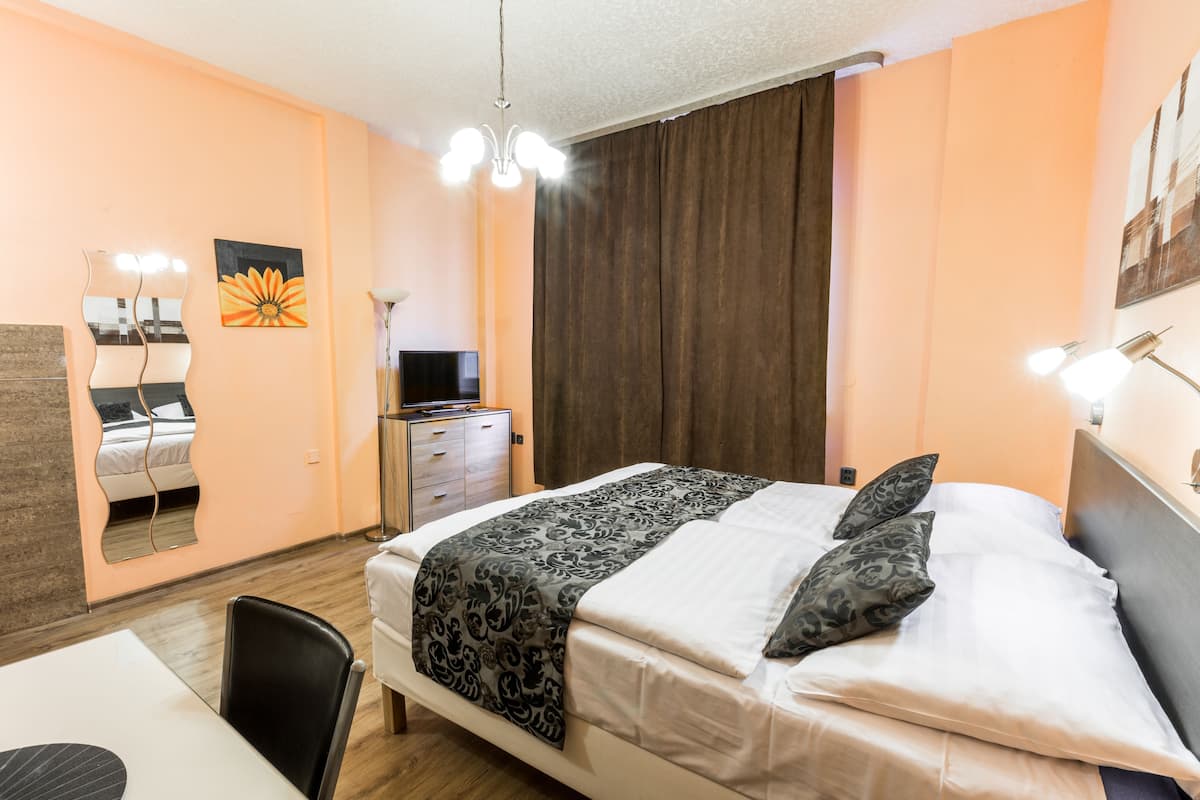 Une chambre d’hôtel comprenant un lit, un bureau, une chaise, une commode, un miroir et une fenêtre avec des rideaux.