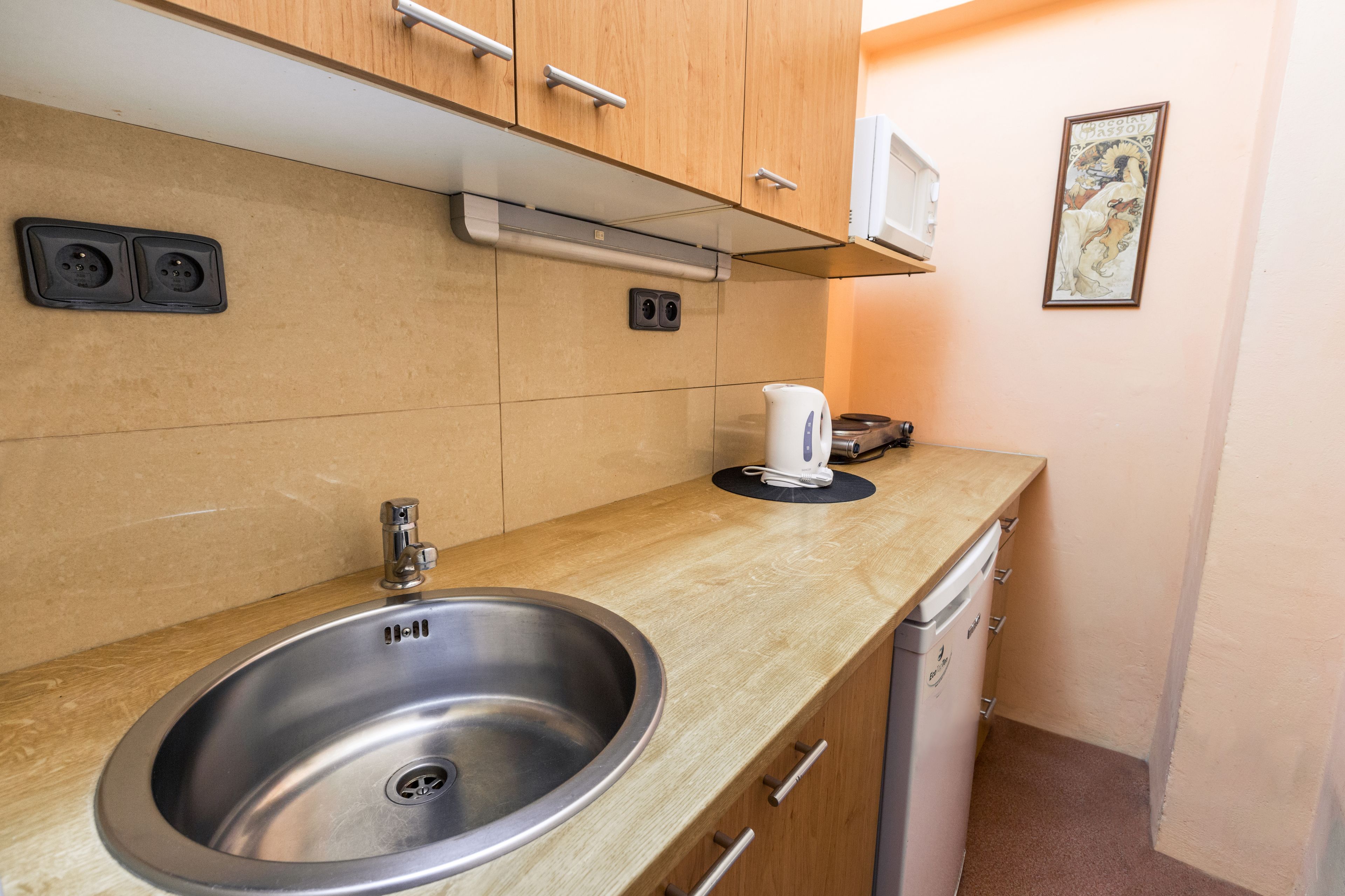 A kitchen with a stainless steel sink, wooden cabinets, a microwave, and a coffee maker.