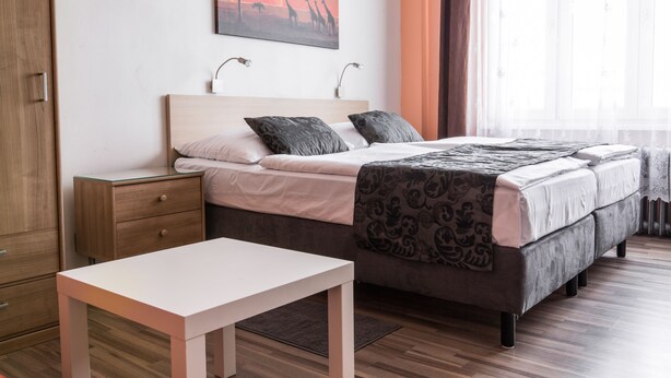 A bedroom with a bed, bedside tables, a nightstand, a window with curtains, and a painting on the wall. - Rezidence Davids (Prague)