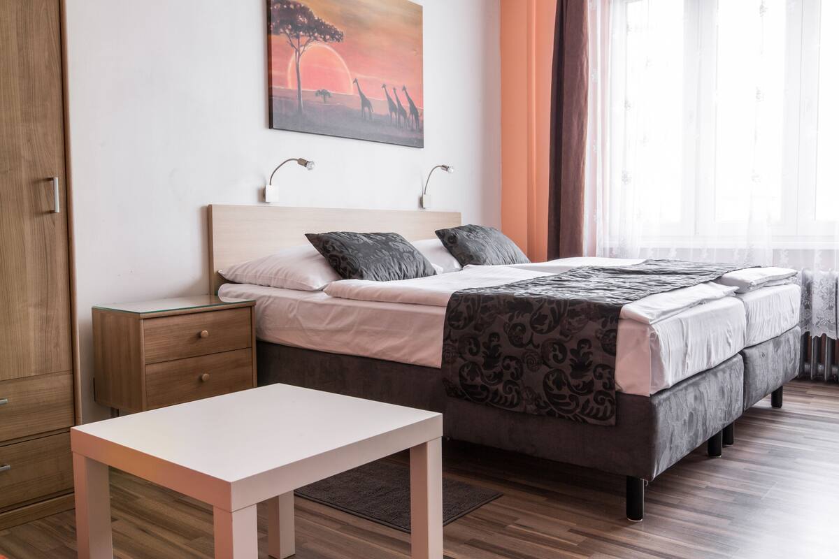 Une chambre à coucher avec un lit, des tables de chevet, une commode, une fenêtre avec des rideaux et un tableau au mur.