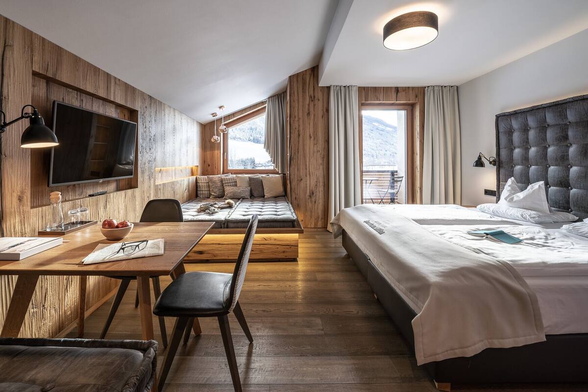 Une chambre d’hôtel moderne avec un mur en bois, un grand lit, un canapé-lit, une table à manger et un téléviseur.