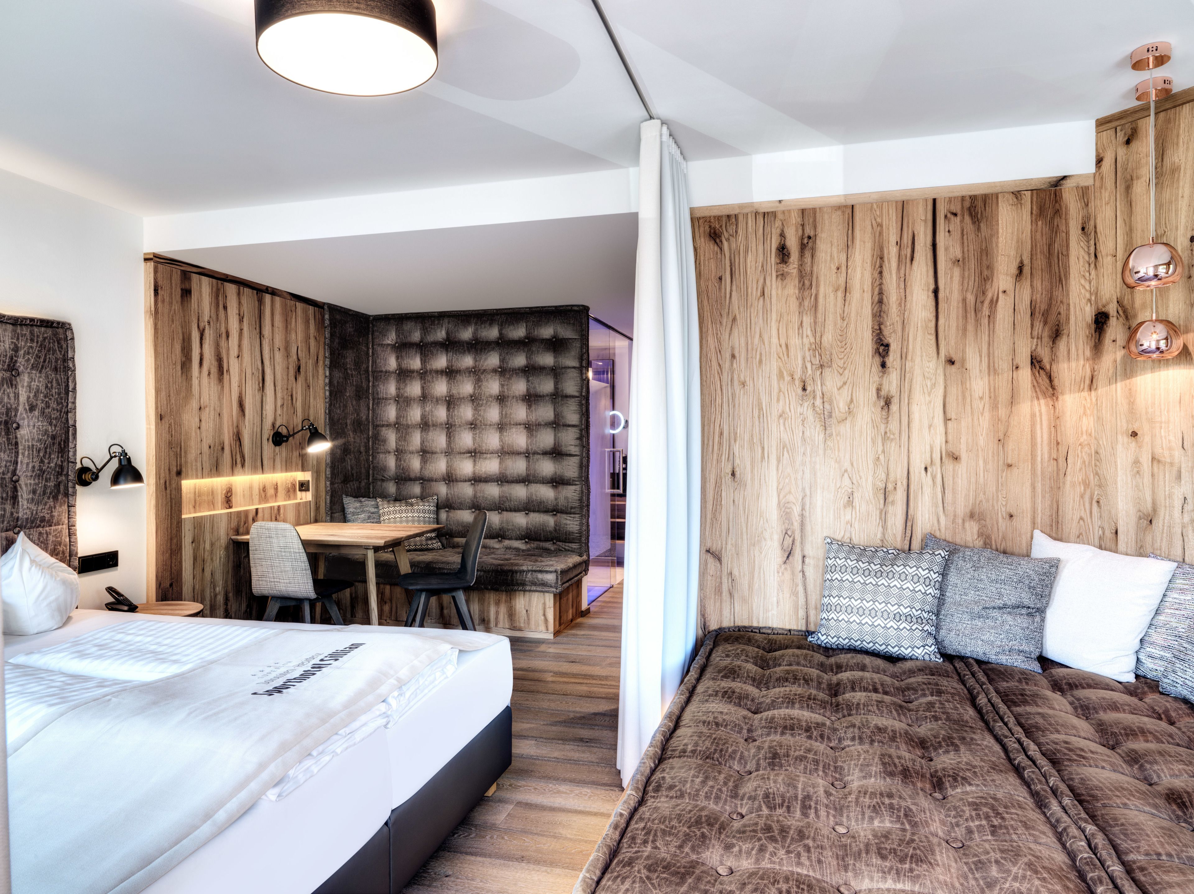 A modern hotel room with a large bed, a small desk, and a seating area with a cushioned bench.