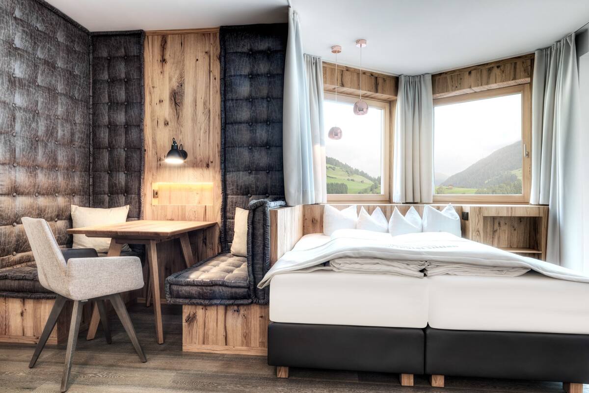 Une pièce confortable avec un lit, un bureau et une chaise, caractérisée par des murs en bois et une vue sur l’extérieur.