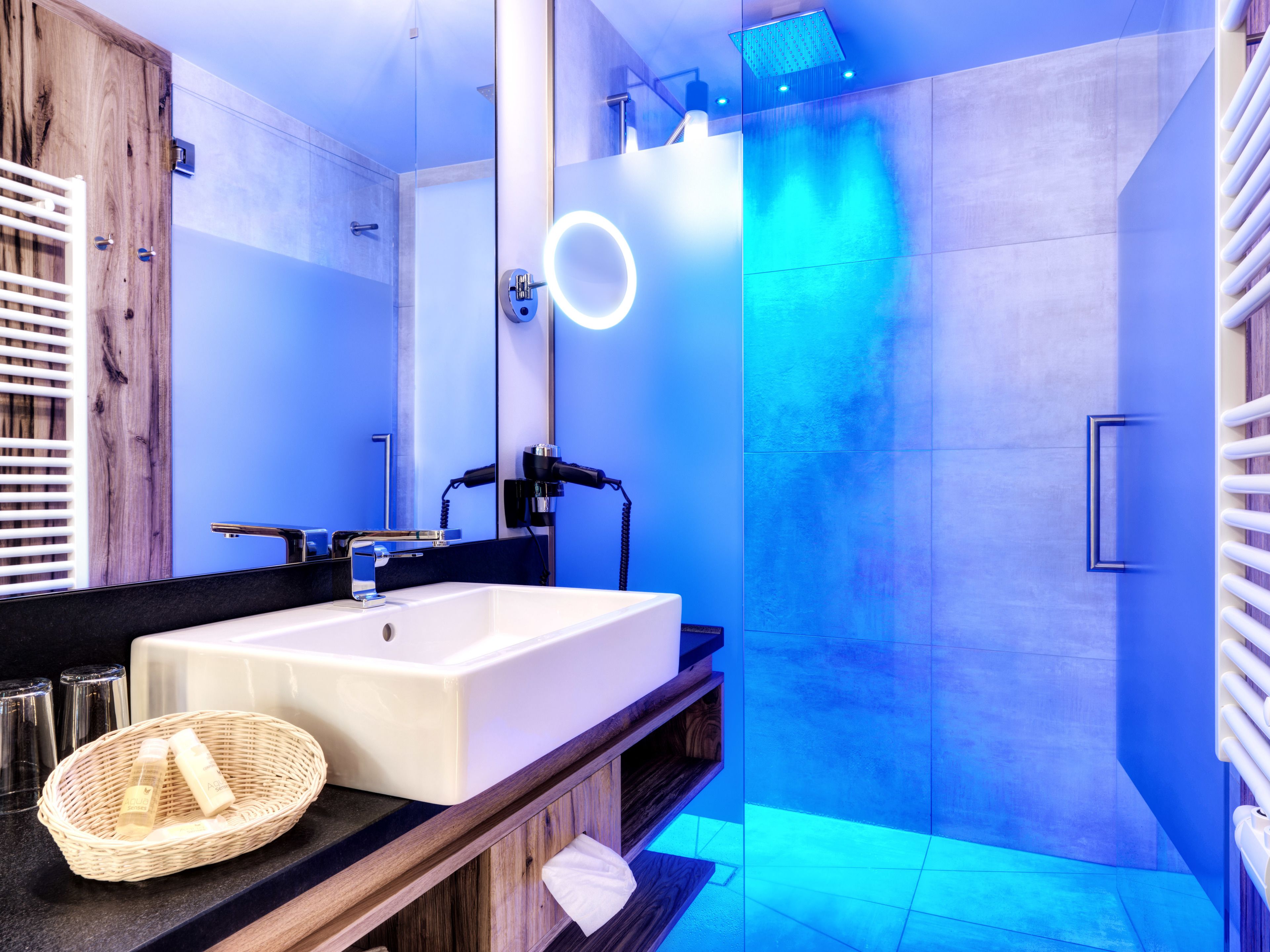 A modern bathroom with a large mirror, a white sink, and a shower with blue lighting.