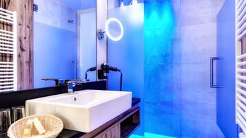 A modern bathroom with a large mirror, a white sink, and a shower with blue lighting.