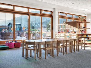 A spacious classroom with large windows, wooden furniture, and educational materials.