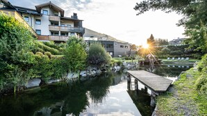 Um edifício moderno com varandas, um píer de madeira e uma superfície aquática calma.