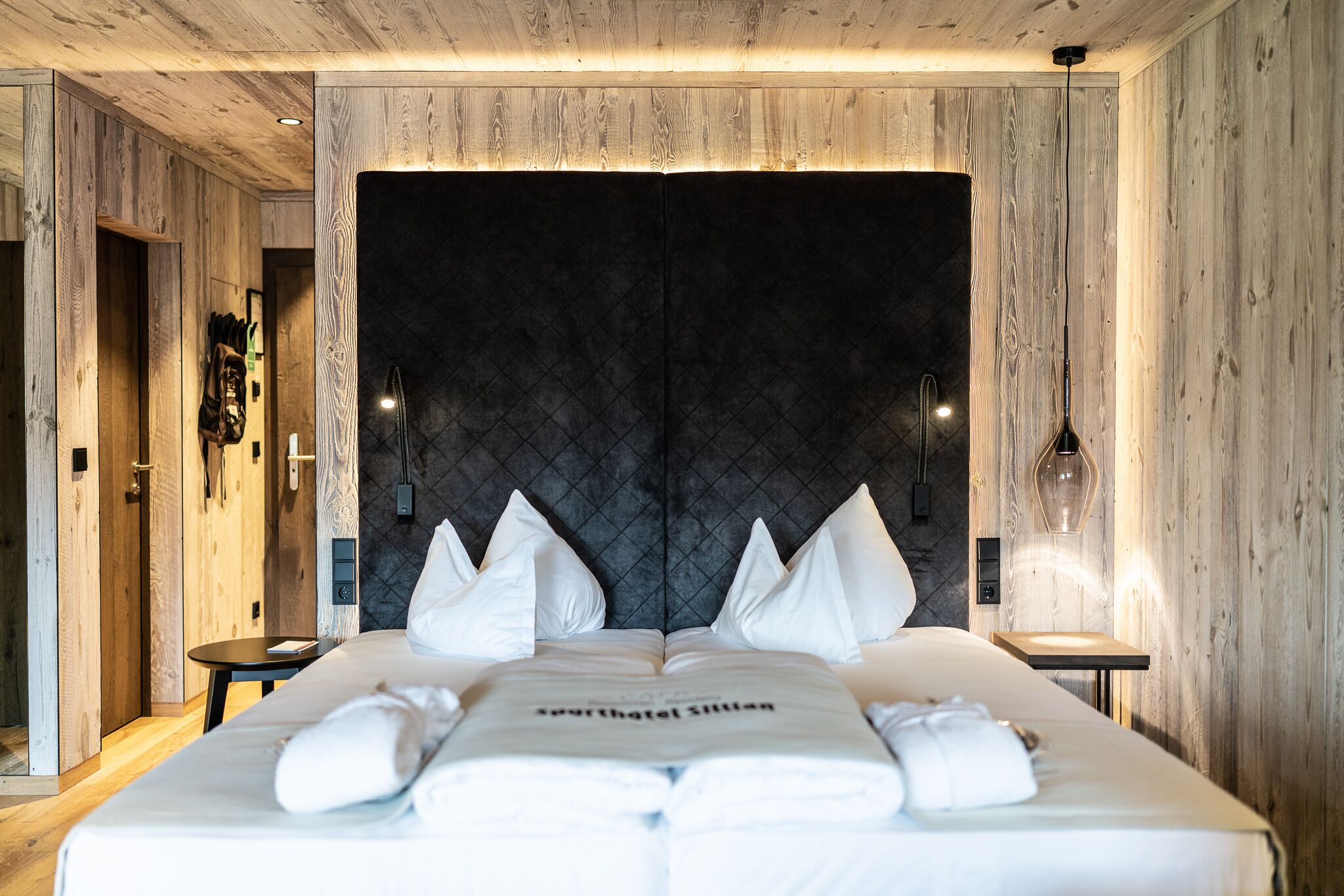 Een keurig opgemaakt bed met witte lakens en kussens, een nachtkastje en een wandlamp.