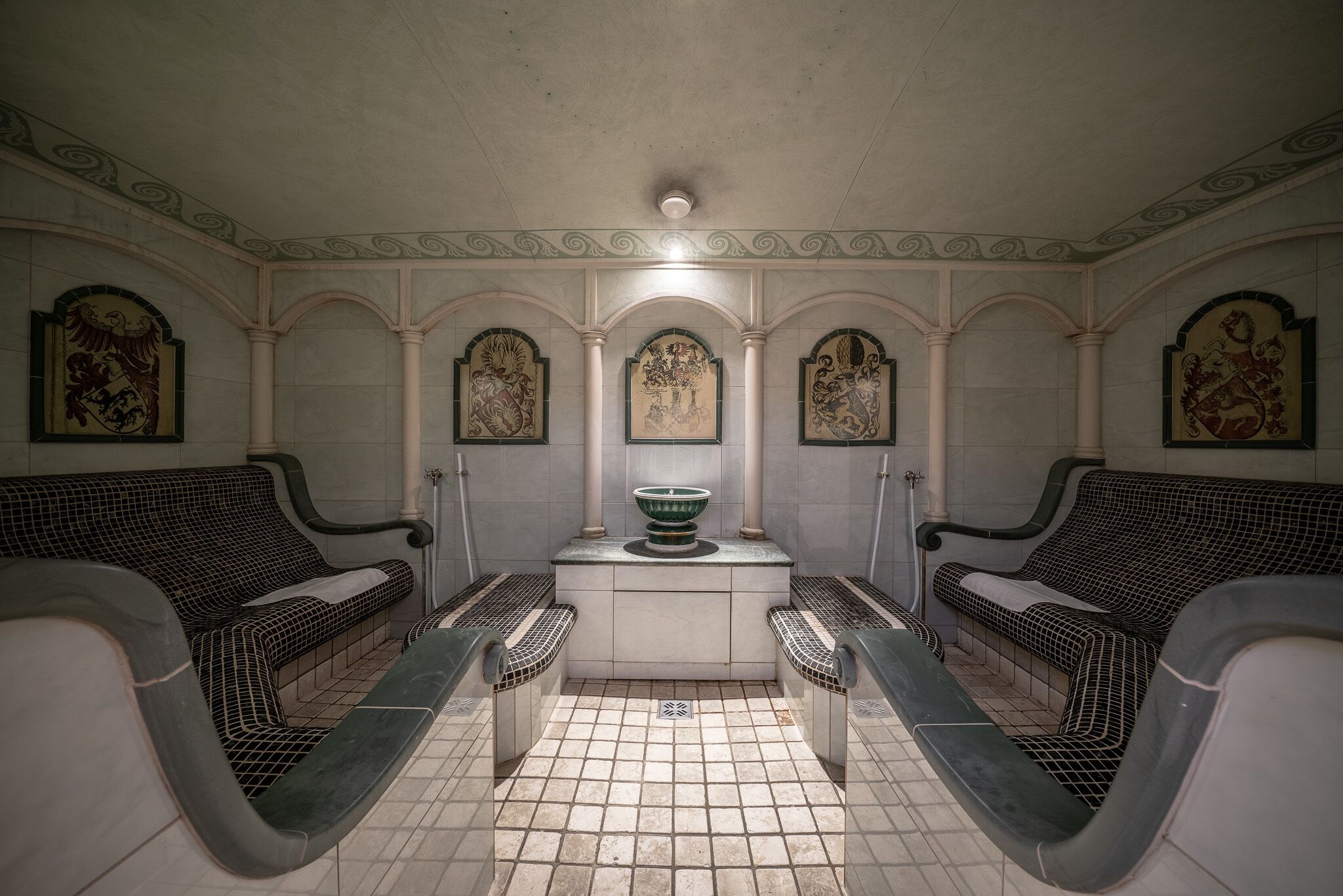 A public sauna with two benches, a central fountain, and ornate wall decorations.