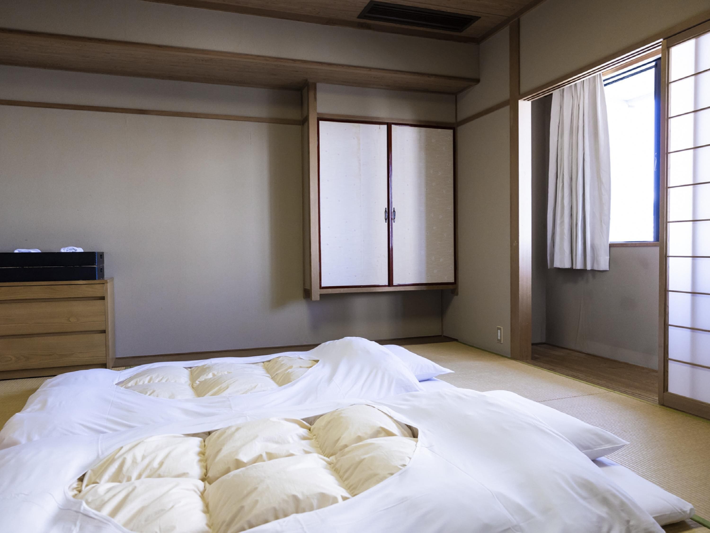 A traditional Japanese-style bedroom with tatami flooring, a low wooden bed, a wardrobe, and a sliding shoji screen.