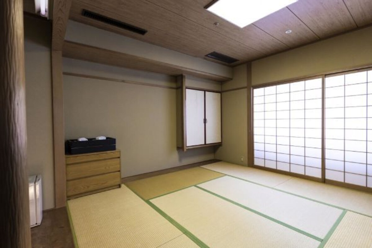 Une pièce de style japonais traditionnel, avec un sol recouvert de tatamis, une porte coulissante et une petite armoire en bois.