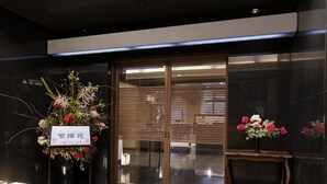 A reception area with a black tiled floor, a wooden bench, and two floral arrangements. - Ariston Hotel Kobe (Kobe)
