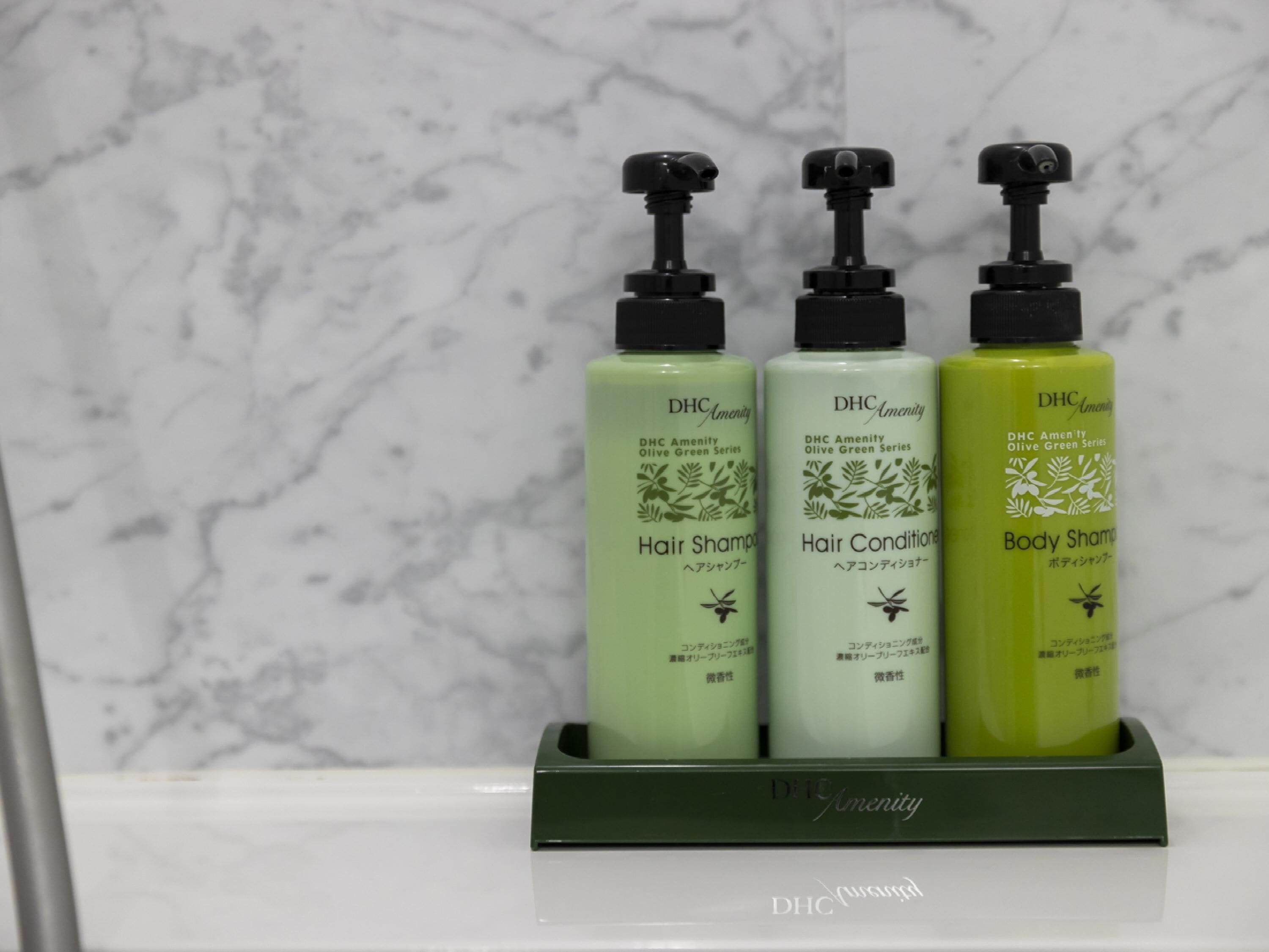 Three bottles of DHC Amenity hair products in a holder.