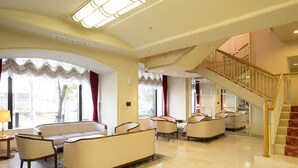 A spacious lobby with a high ceiling, a staircase, and a seating area with sofas and chairs. - Ariston Hotel Kobe (Kobe)
