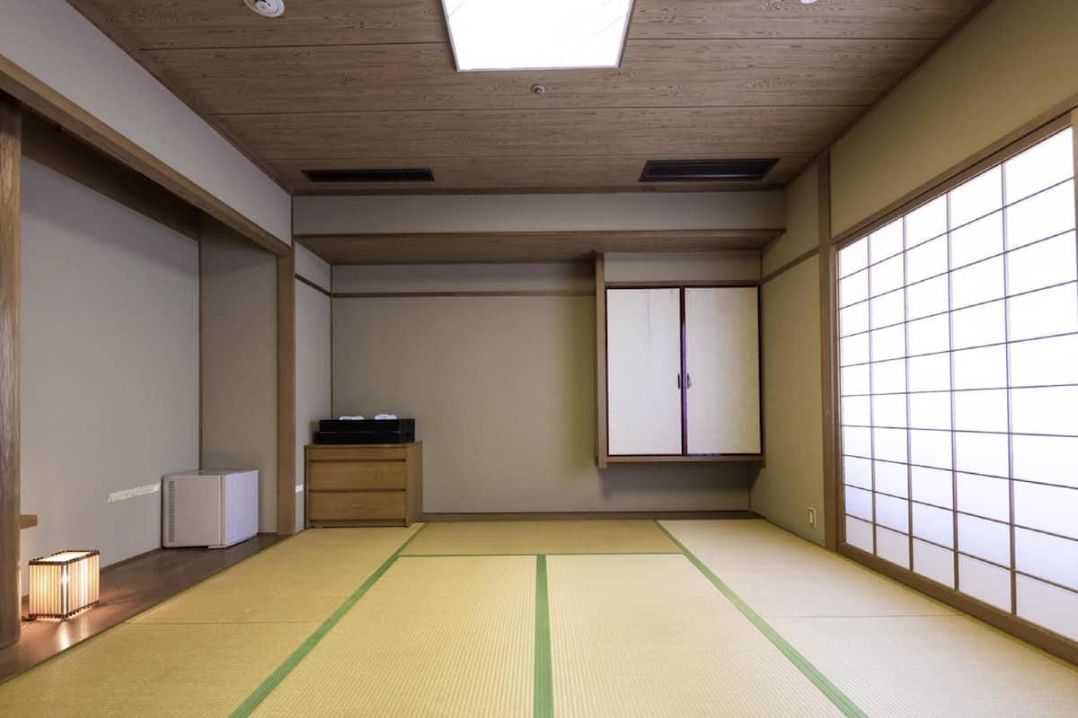 A traditional Japanese room with tatami flooring, a low wooden ceiling, and sliding doors.