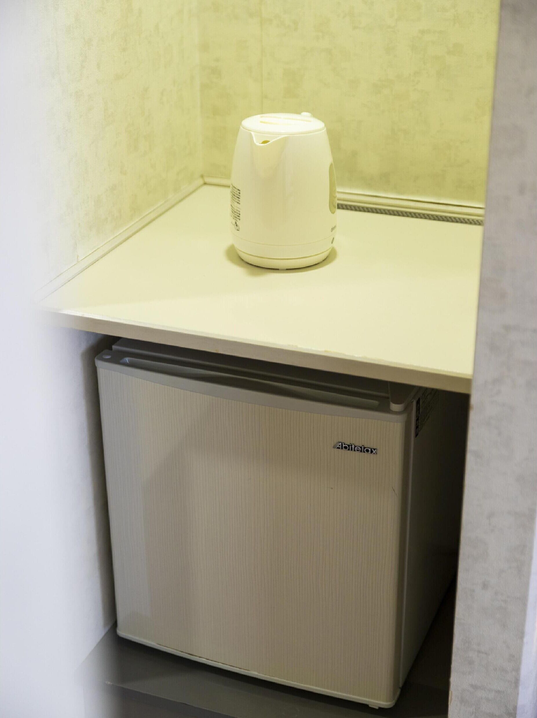 Una kitchenette compacta con un refrigerador pequeño y una cafetera sobre la encimera.