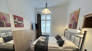 Quarto de hotel com duas camas, uma televisão, uma janela com cortinas e obras de arte nas paredes.