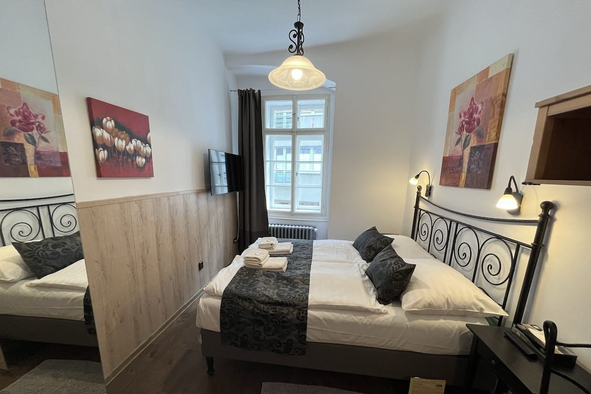 Ein Hotelzimmer mit zwei Betten, einem Fernseher, einem Fenster mit Vorhängen und Bildern an den Wänden.