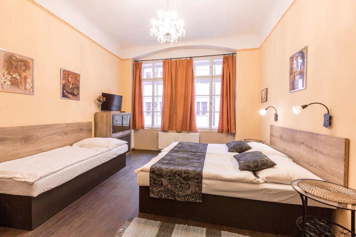 Ein Hotelzimmer mit zwei Einzelbetten, einem Holzkopfstück, einer Chandelüster, einem kleinen Tisch und Bildern an den Wänden.