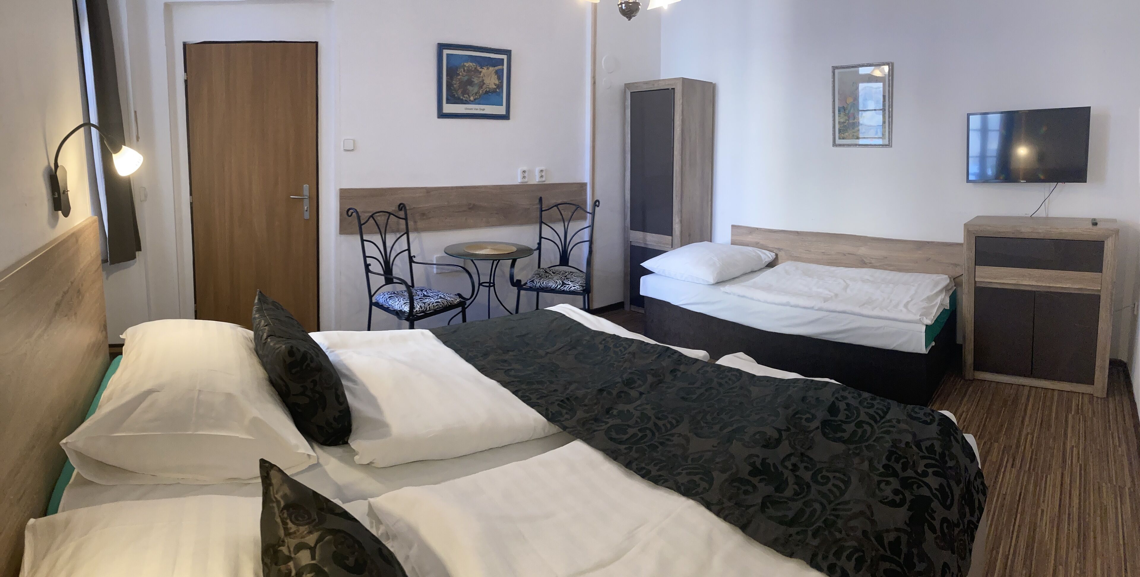 A hotel room with two beds, a small table with chairs, a television, and a wardrobe.