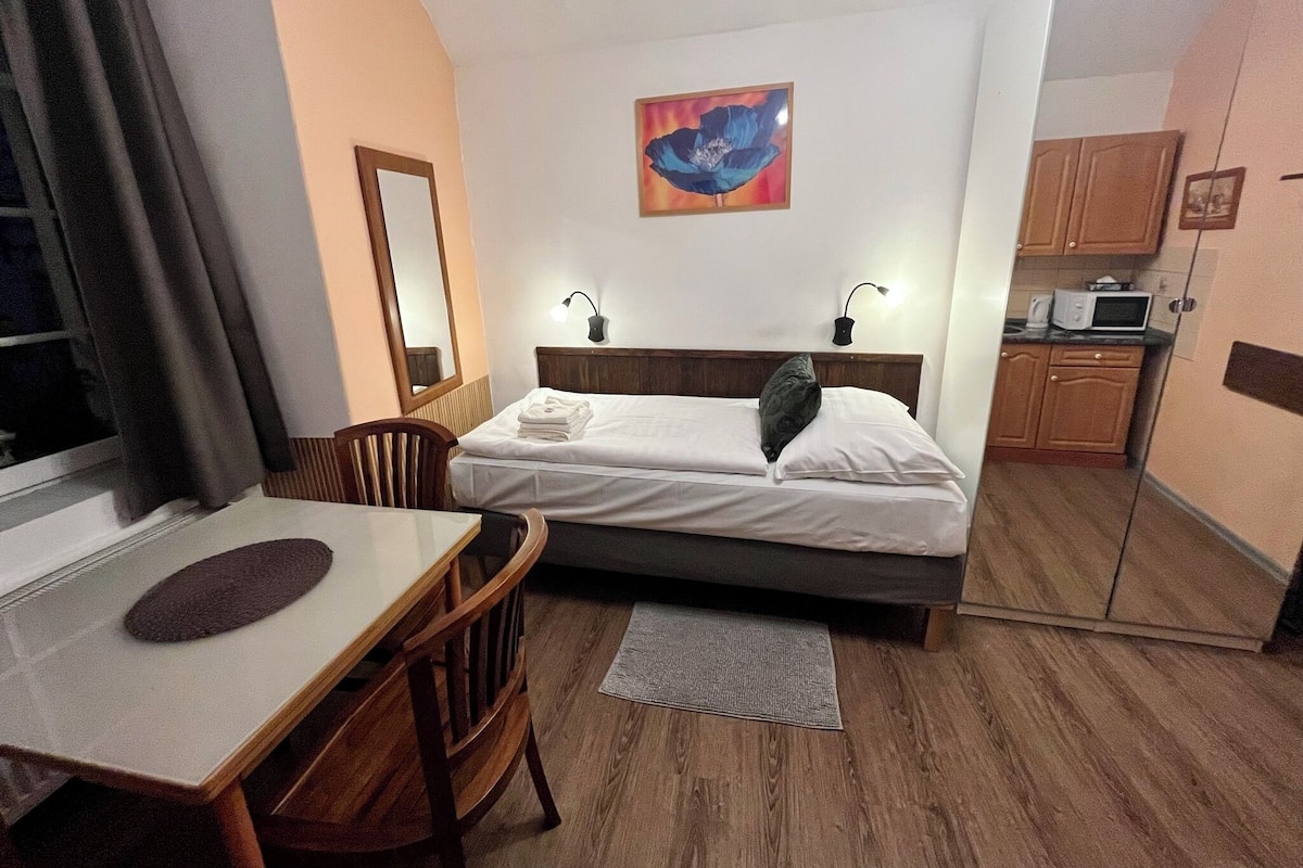 Ein Hotelzimmer mit Bett, Nachttisch, Stuhl und einer kleinen Küchenzeile.