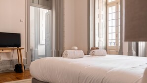 Habitación de hotel con una cama grande, un televisor sobre un mueble de madera y vistas al exterior a través de ventanas amplias.