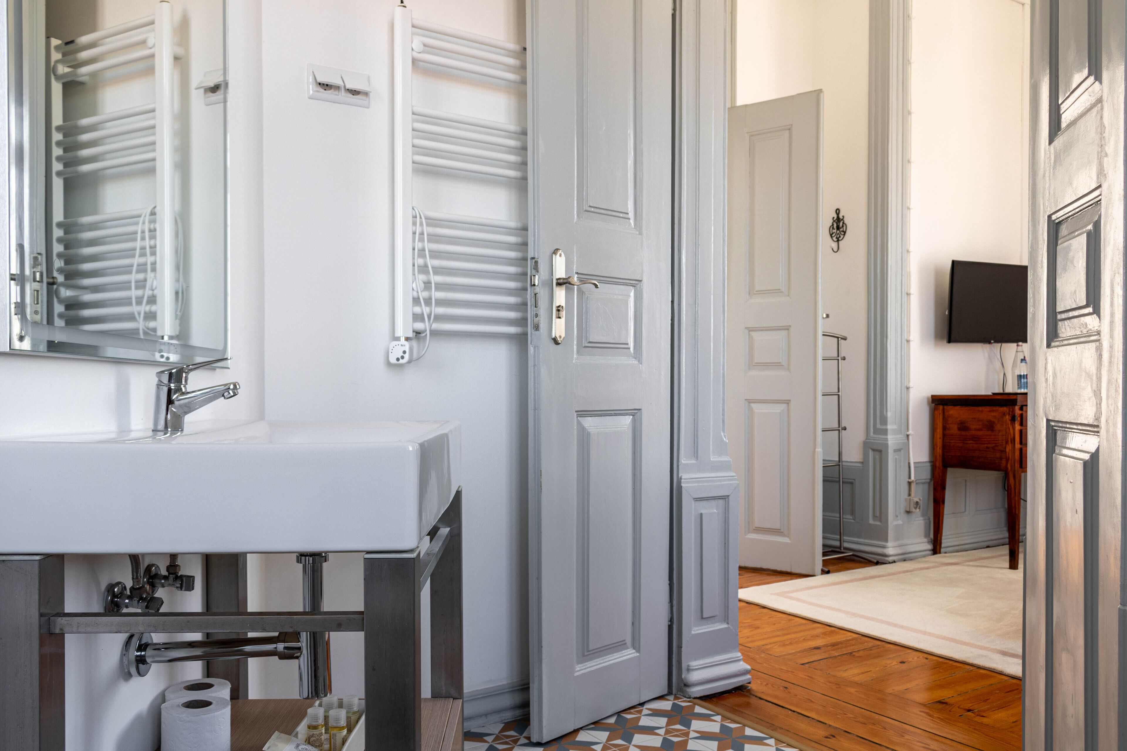 Un baño con un lavamanos blanco, toalleros y una puerta que da a otra habitación.