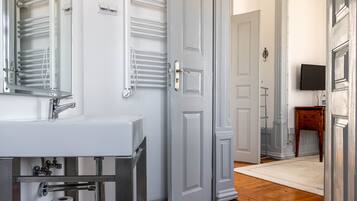 Un baño con un lavamanos blanco, toalleros y una puerta que da a otra habitación.