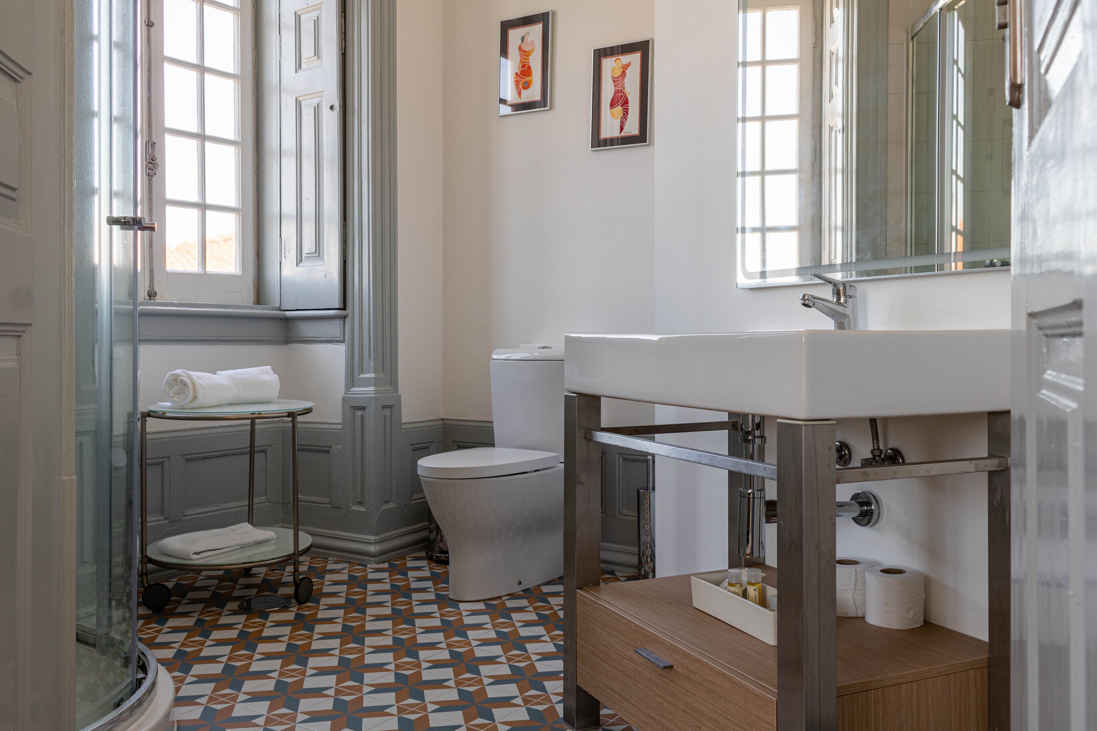 Baño con inodoro, lavabo y ducha. Hay toallas en un perchero y un espejo sobre el lavabo.