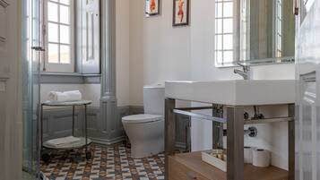 Baño con inodoro, lavabo y ducha. Hay toallas en un perchero y un espejo sobre el lavabo.