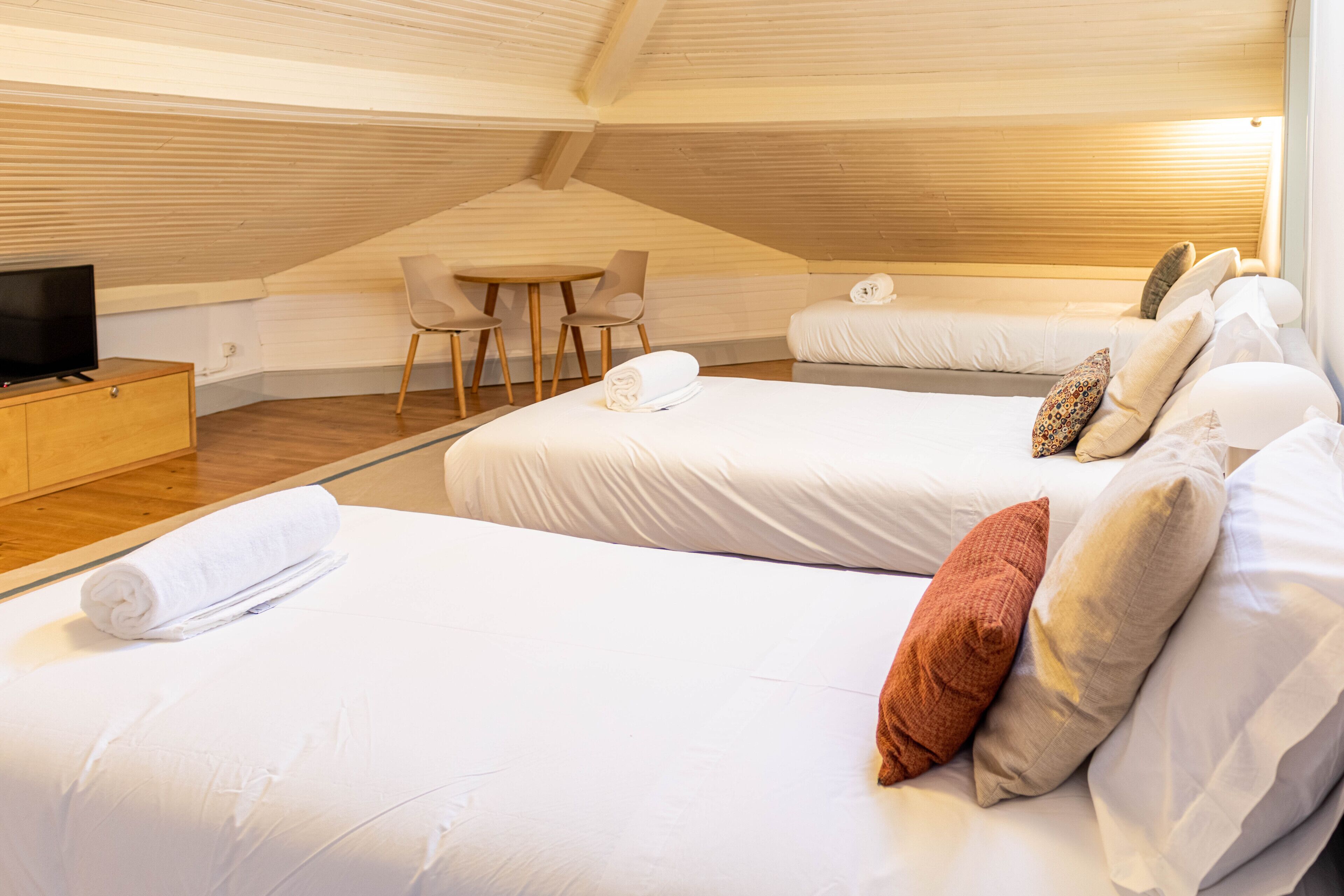 A cozy attic bedroom with two beds, a TV, a small table, and chairs.