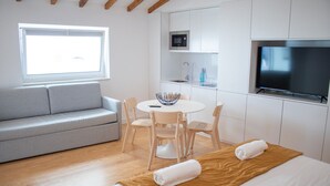 Una habitación de hotel moderna con sofá, una mesa de comedor con sillas, televisor y zona de cocina con microondas y fregadero.