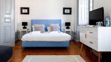 Un dormitorio con una cama azul, mesitas de noche blancas, un aparador blanco y un televisor.