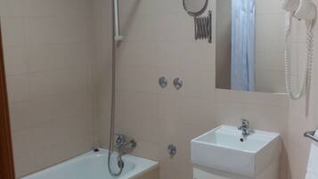 A bathroom with a bathtub, a sink, a toilet, a showerhead, a mirror, and a hairdryer.